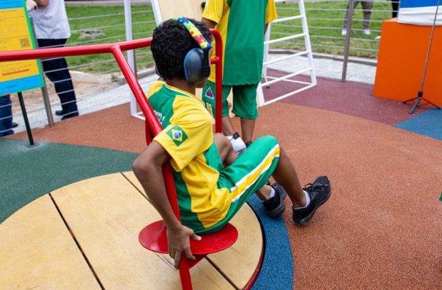 Criança com abafadores sensoriais brincando no carrossel do Parque Girassol